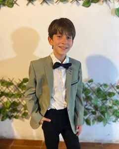 Niño con saco verde salvia y moño negro, sonriendo